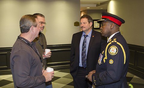 Four men, one in TPS uniform, stand together talking