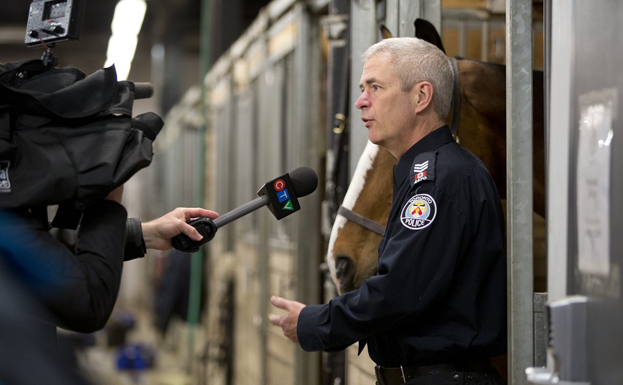 A man in TPS uniform holding a horse's reins while talking to a microphone and video camera