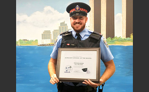Man in a uniform holding an award plaque with his name on it as an auxiliary officer of the month
