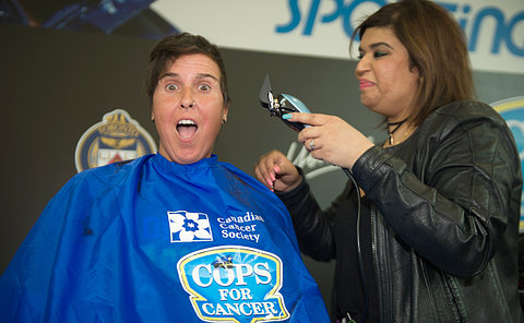 A woman in a barber's smock is shaved by another woman with electric shears