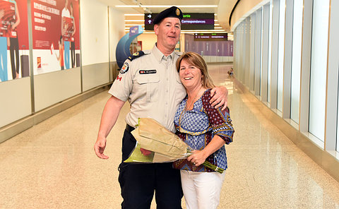 Man in a uniform and a woman holding a bouquet of flowers, hugging.
