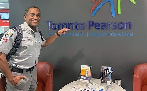 Man in a police uniform standing in a lounge and pointing at a sign Toronto Pearson International Airport