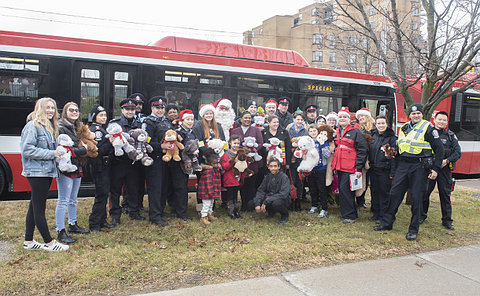 A group of people in front of a TTC bus holding toys