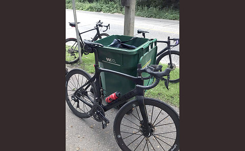 Several bicycles parked around a large green waste bin