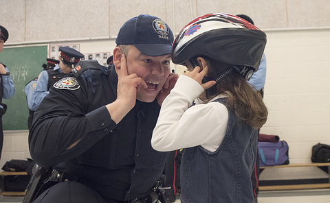 A girl in a bicycle helmet with a man in TPS uniform crouched down