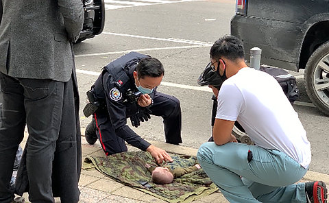 A police officer crouched over a baby on a sidewalk