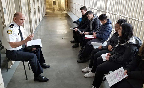 A man in TPS uniform sitting in a corridor with students