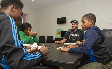 A man in TPS uniform playing dominoes with teens at a table