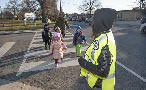 A group of kids and adult crossing the street between two kids in yellow vests